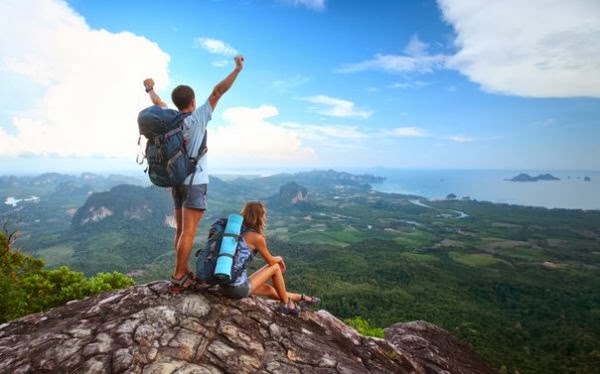 Парень и девушка на вершине холма с рюкзаками за плечами